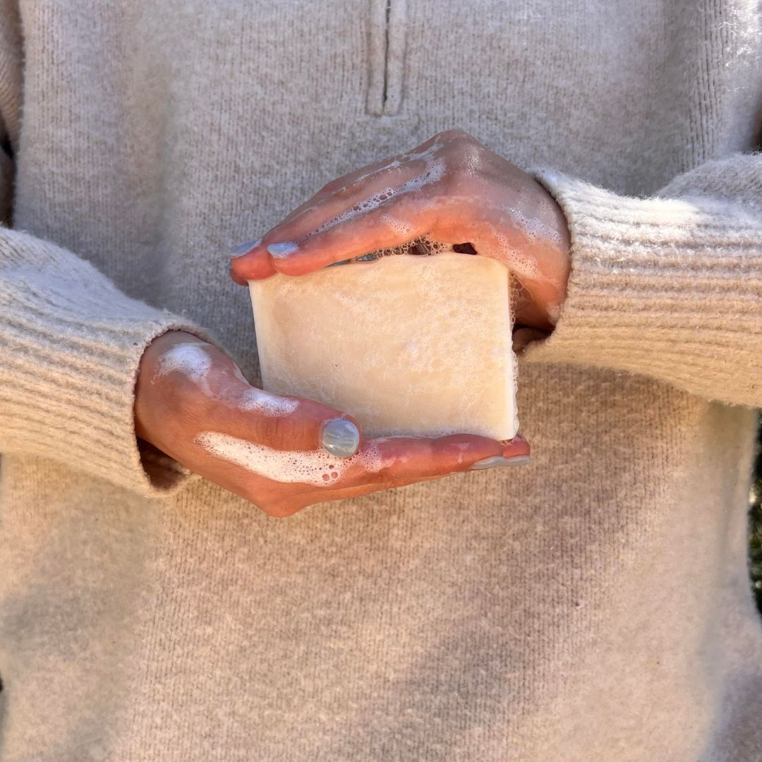 Person holding a large, lathered bar of tallow soap with both hands, dressed in a cosy, beige sweater