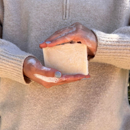 Person holding a large, lathered bar of tallow soap with both hands, dressed in a cosy, beige sweater