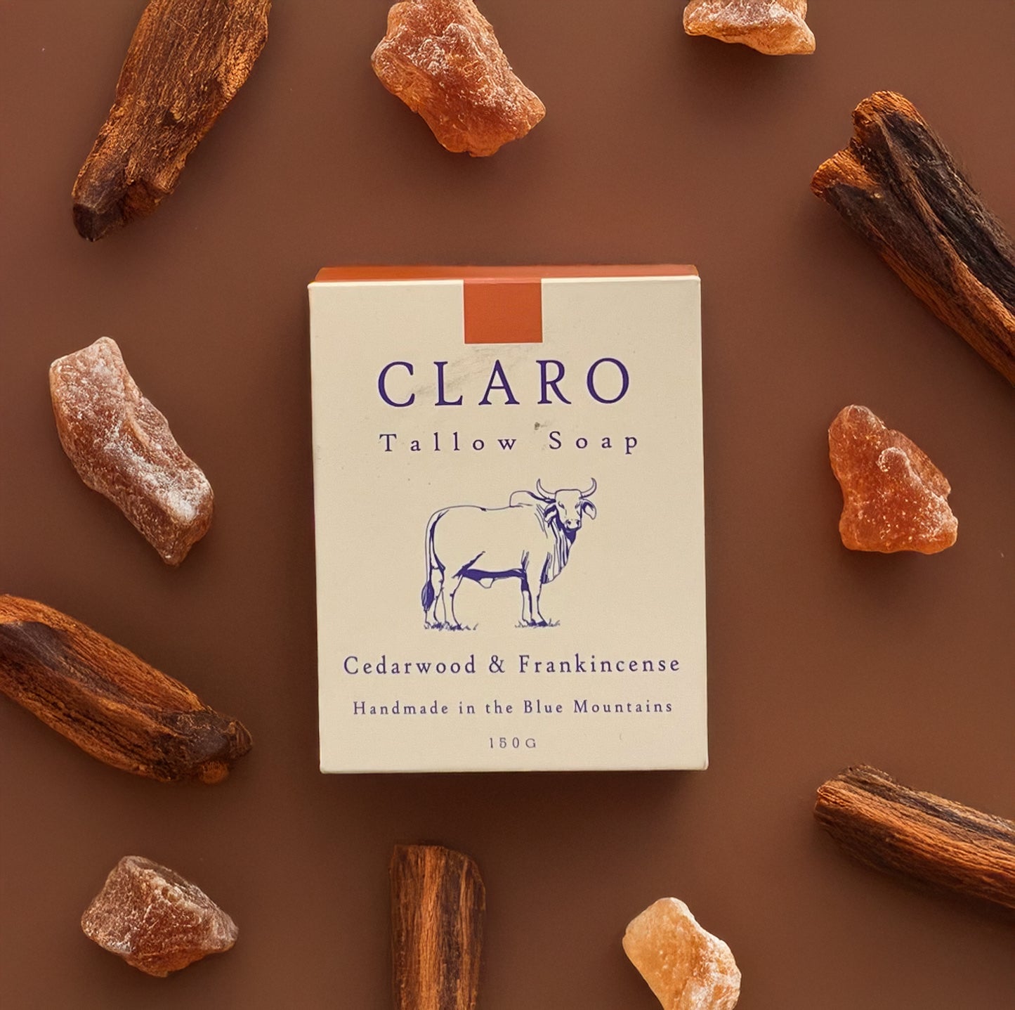 Claro Tallow Soap box labeled 'Cedarwood & Frankincense,' surrounded by pieces of cedarwood and frankincense resin on a brown background