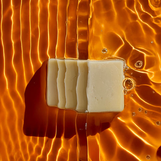 Bar of Claro soap submerged in water with golden ripples, creating a warm, radiant effect across the surface.