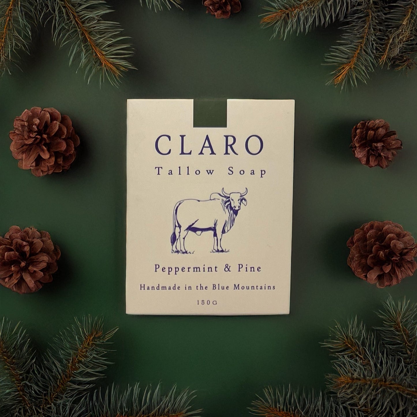 Claro Tallow Soap box labeled 'Peppermint & Pine,' surrounded by pine branches and pinecones on a green background.